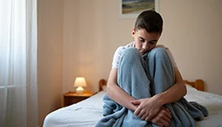 Парень сидит на кровати обняв колени